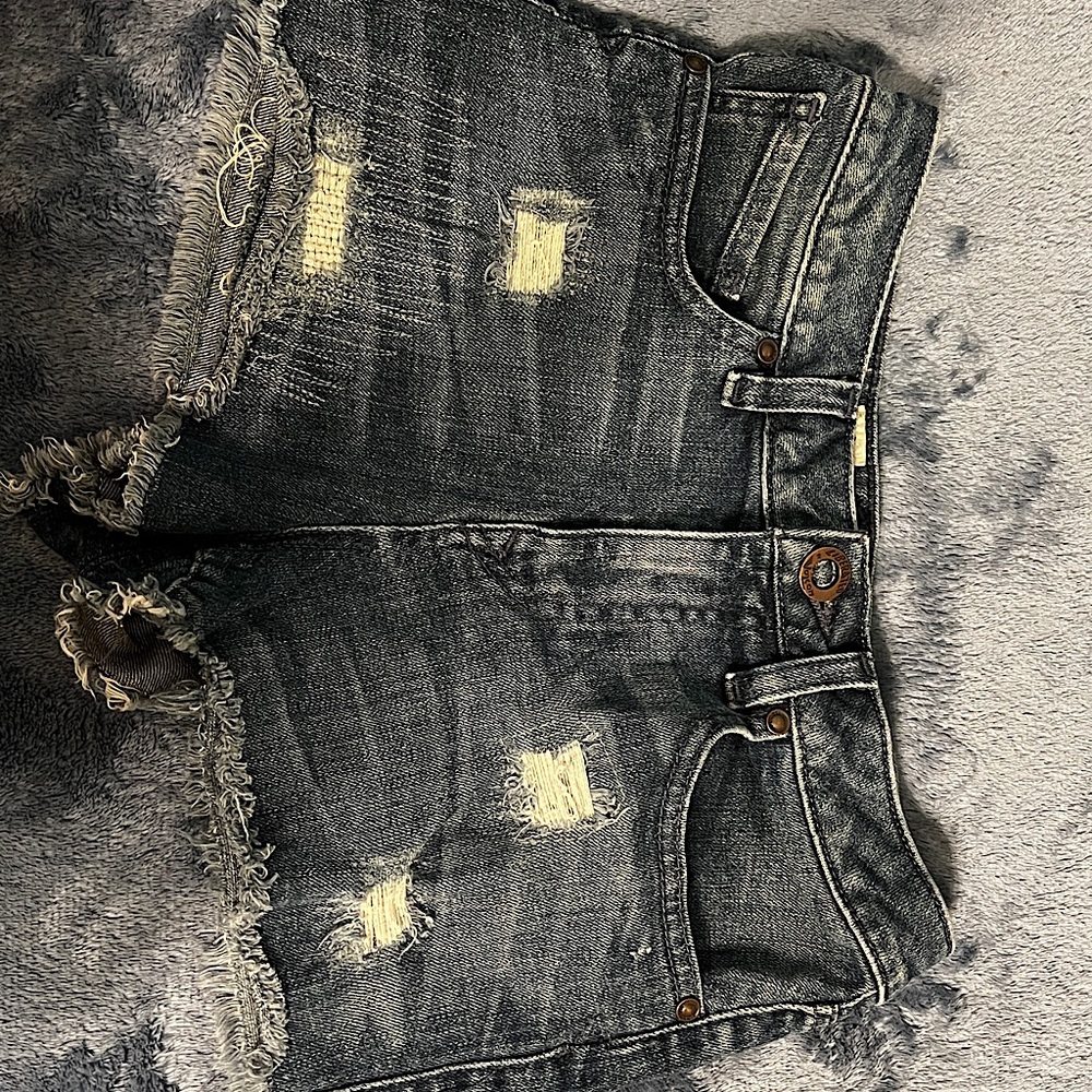 Jean shorts have rips in the front and pattern stitching on lower thigh